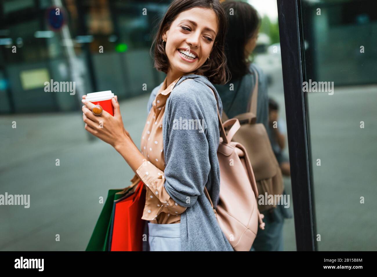 Une jeune femme heureuse à boire du café et à marcher avec des sacs après avoir fait du shopping en ville. Banque D'Images