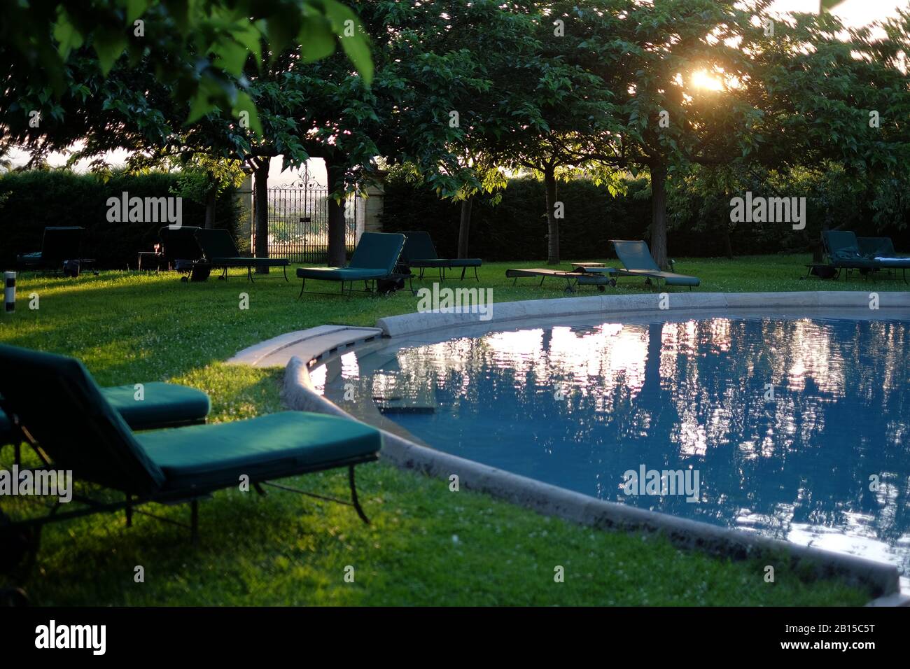 Des salons vides au bord de la piscine et une piscine ronde à l'ombre de la fin de l'après-midi avec le soleil derrière les cerisiers au luxueux Château de Bagnols France Banque D'Images