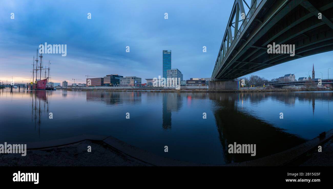 Longue exposition de l'Überseestadt à Brême, Allemagne avec bâtiment de bureau, bateau à voile et réflexion parfaite sur le weser pendant l'heure bleue, dernier Banque D'Images