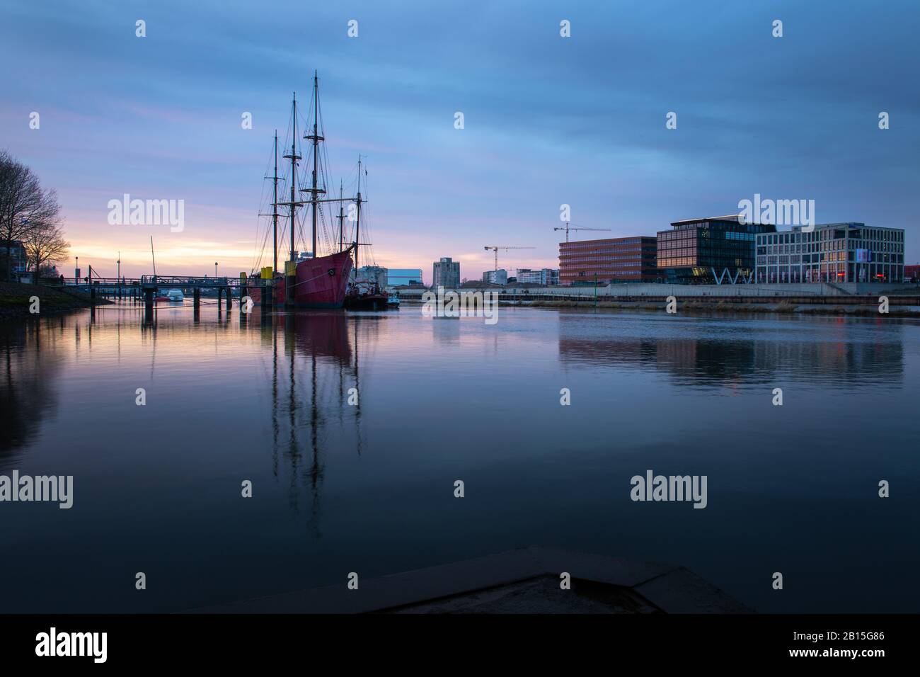 Longue exposition de l'Überseestadt à Brême, Allemagne avec bâtiment de bureau, bateau à voile et réflexion parfaite sur le weser pendant l'heure bleue, dernier Banque D'Images
