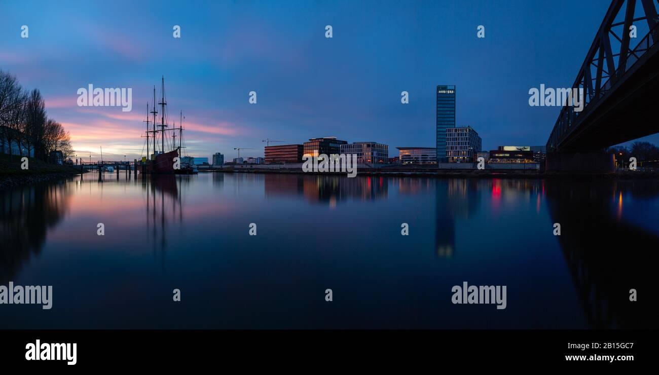 Longue exposition de l'Überseestadt à Brême, Allemagne avec bâtiment de bureau, bateau à voile et réflexion parfaite sur le weser pendant l'heure bleue, dernier Banque D'Images