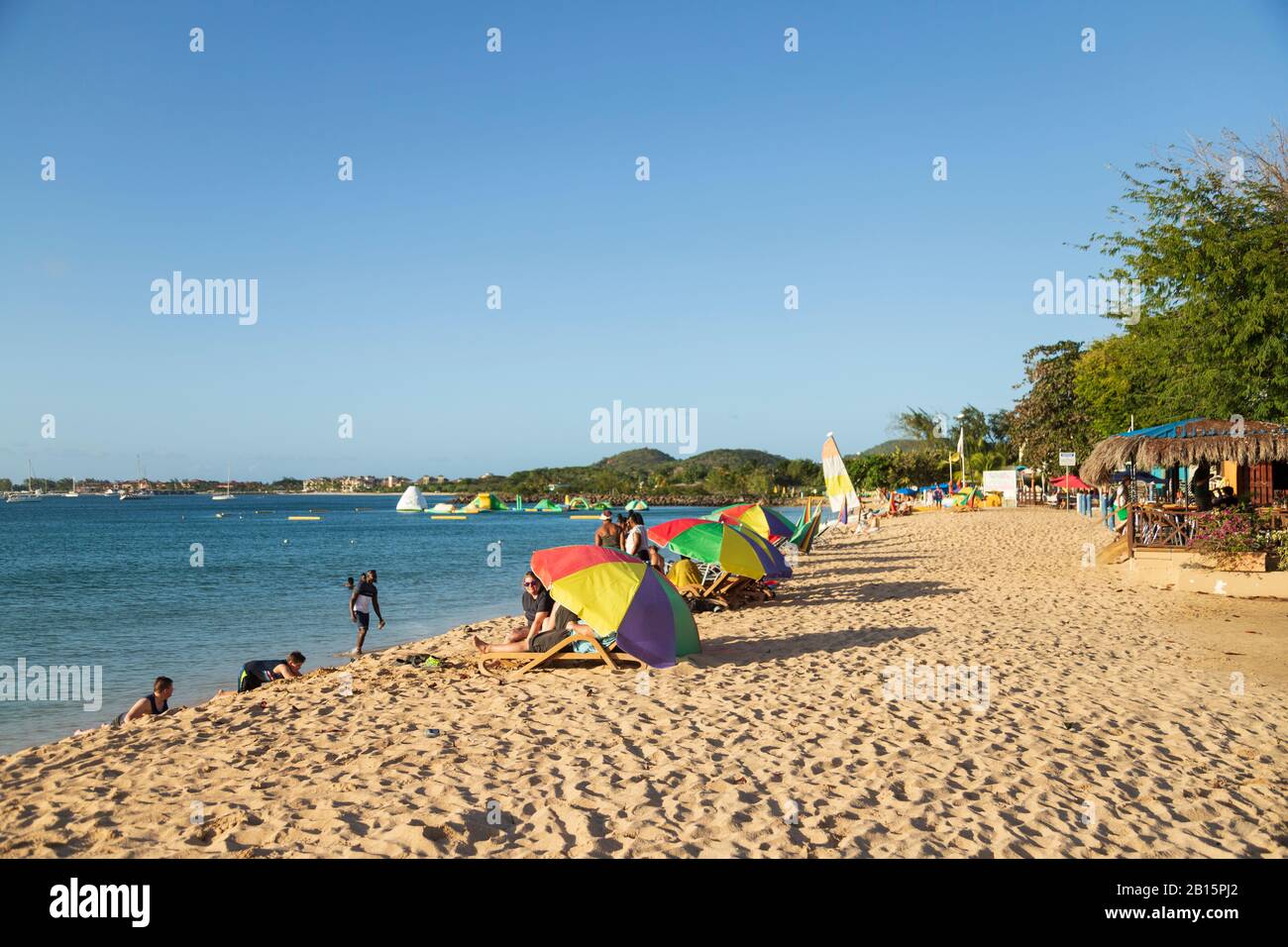 Plage de sable une journée ensoleillée avec des gens qui s'amusent sur la plage au soleil et se baignent en mer et se prometent sous les parasols Banque D'Images