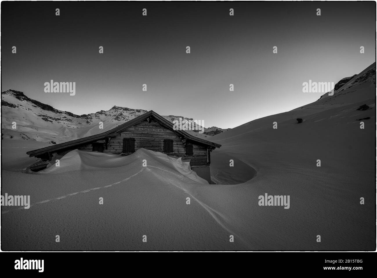 Photo en noir et blanc d'un chalet dans la neige au crépuscule Banque D'Images