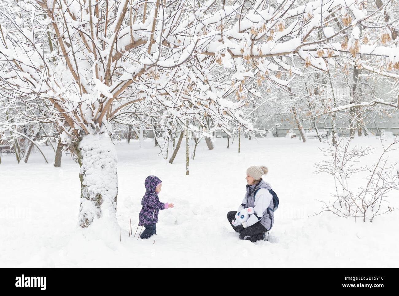 Petit enfant avec la mère marcher dans un parc enneigé en hiver. Une fillette joue dans la neige. Promenades en famille pendant la chute de neige. Banque D'Images