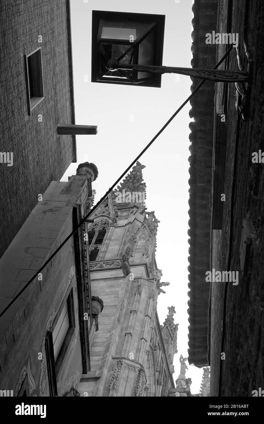 Une image monochrome regardant vers le haut à travers une rue étroite côté ville à une cathédrale catholique romaine Banque D'Images