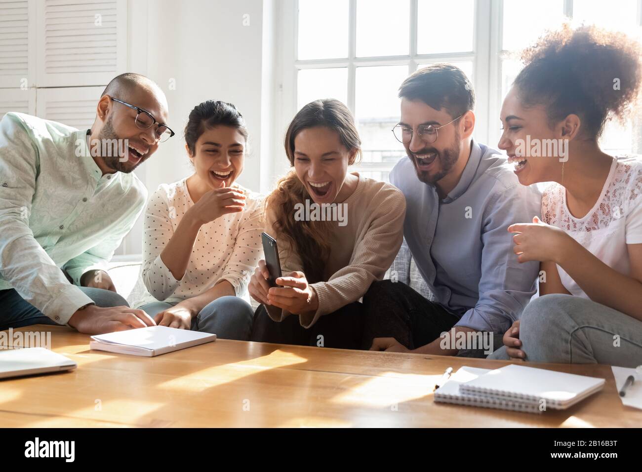 Cinq amis multiethniques riant s'amuser à l'aide d'un smartphone Banque D'Images