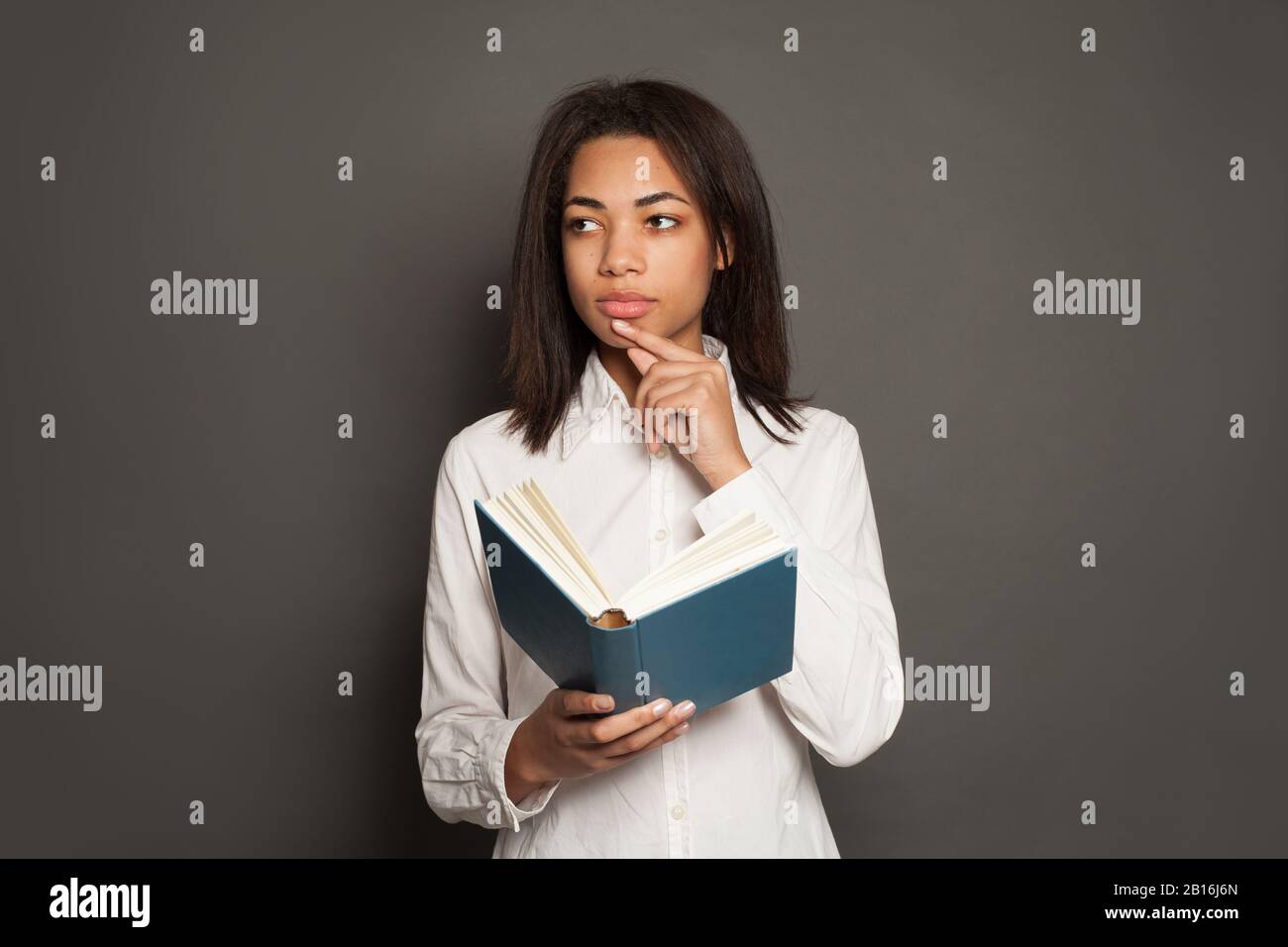 Pensée mixte race ethnicité femme noire étudiant en chemise blanche avec livre sur fond gris Banque D'Images