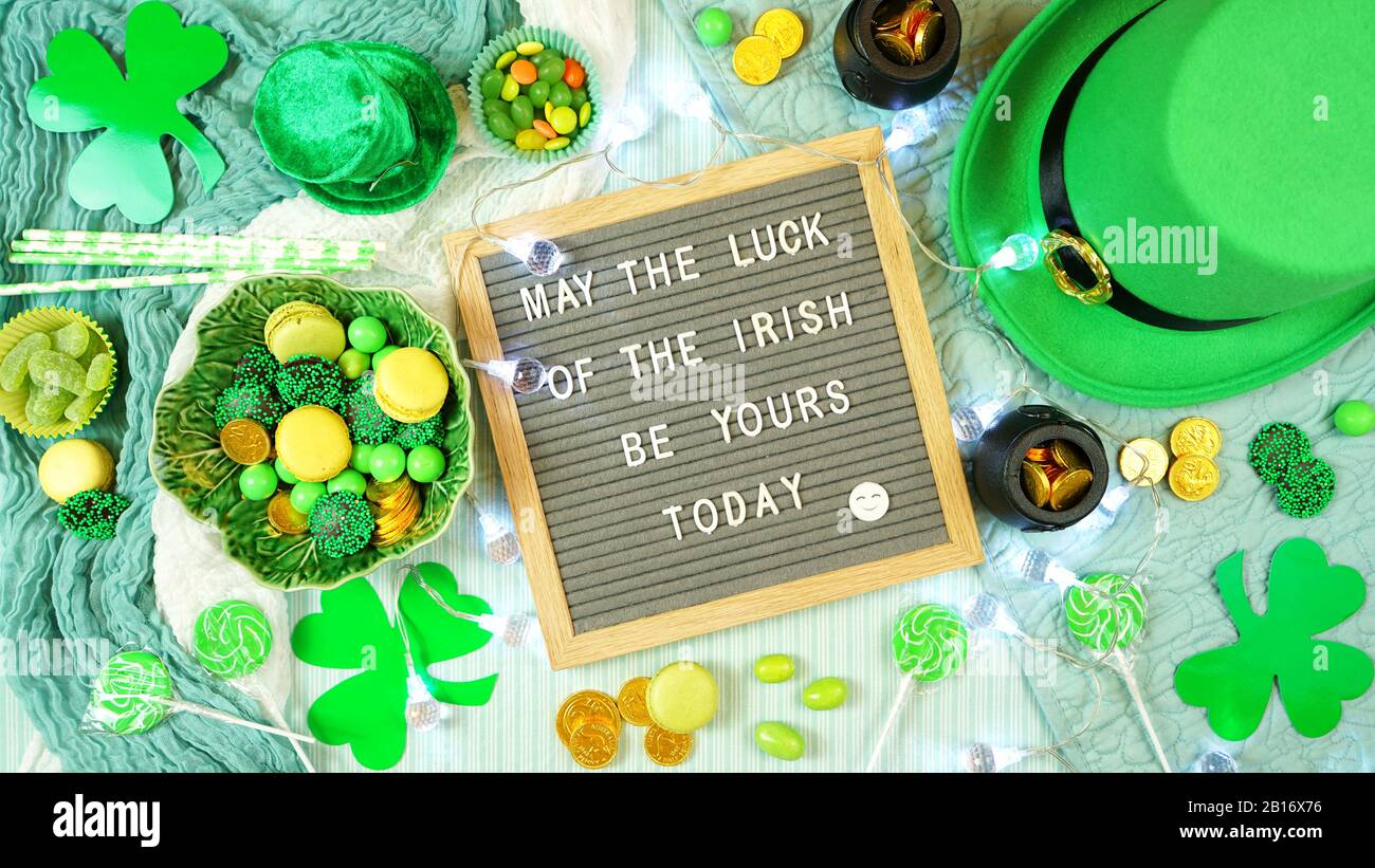 Style hygge St Patrick's Day composition créative plat disposition avec chapeau de leprechaun, pièces de chocolat, shamrocs et bonbons avec planche à lettres dans le lit. Banque D'Images