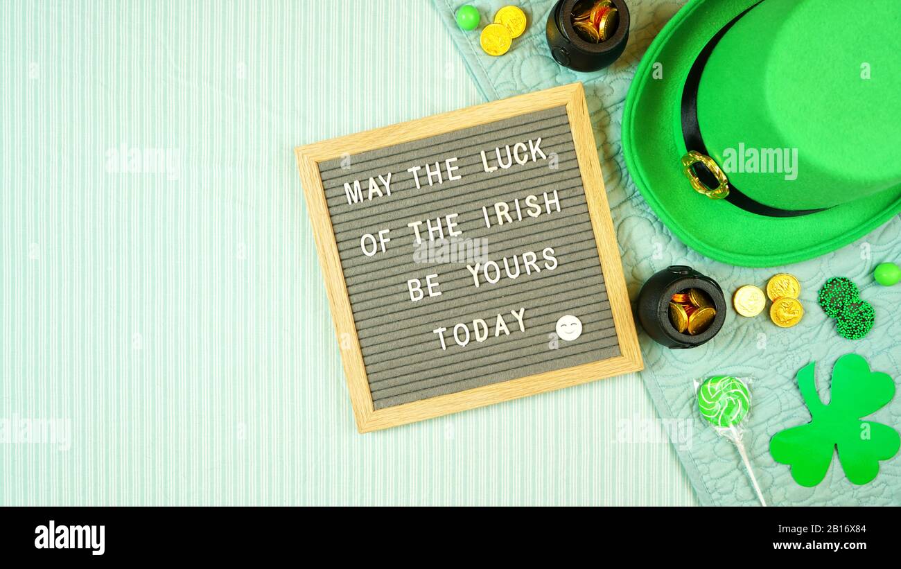 La décoration de style hygge de St Patrick's Day avec un chapeau de leprechaun, des pièces de chocolat, des shamrocs et des bonbons avec un tableau à lettres dans le lit, Banque D'Images