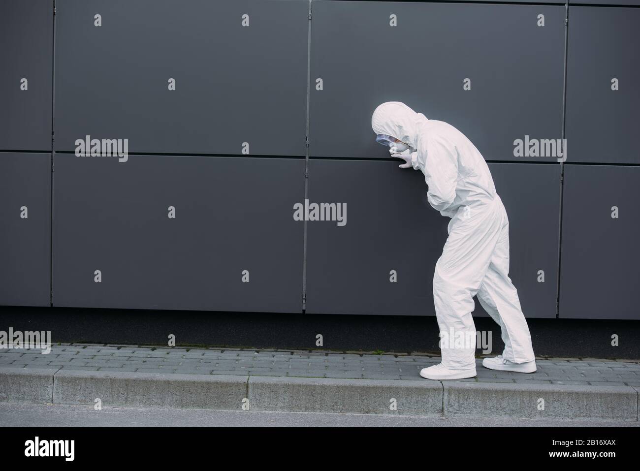 l'épidémiologiste asiatique de la combinaison hazmat s'est penchée sur le mur tout en souffrant de douleurs abdominales symptomatiques Banque D'Images