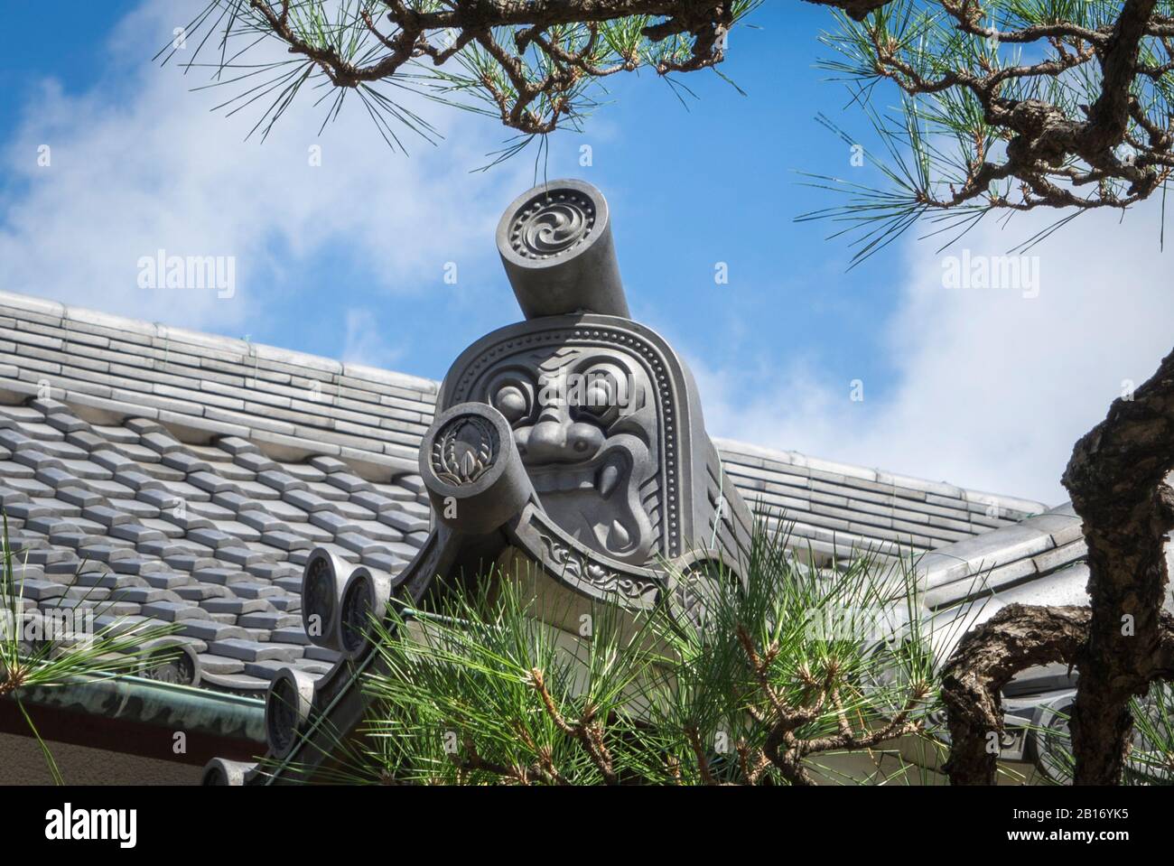 Toit traditionnel d'un temple japonais, Nagoya, Japon, tuile de toit ornée en forme d'oni encadrée par des branches de pin et un ciel bleu d'été Banque D'Images