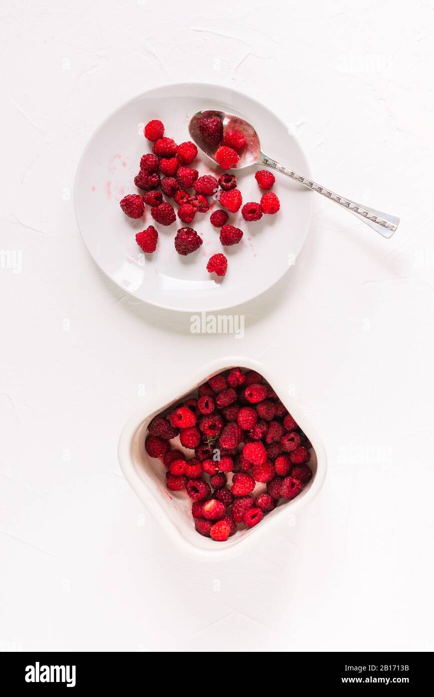 Plaque, cuillère et récipient avec framboises sur fond blanc. Baies fraîches d'été. Saine alimentation Banque D'Images