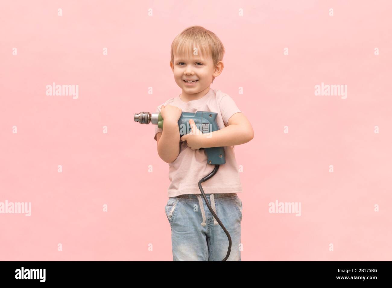 Happy boy se tient et tient une vraie perceuse électrique de couleur bleue. Pour les articles sur les appareils et les outils, leur facilité d'utilisation et l'éducation des enfants. Banque D'Images