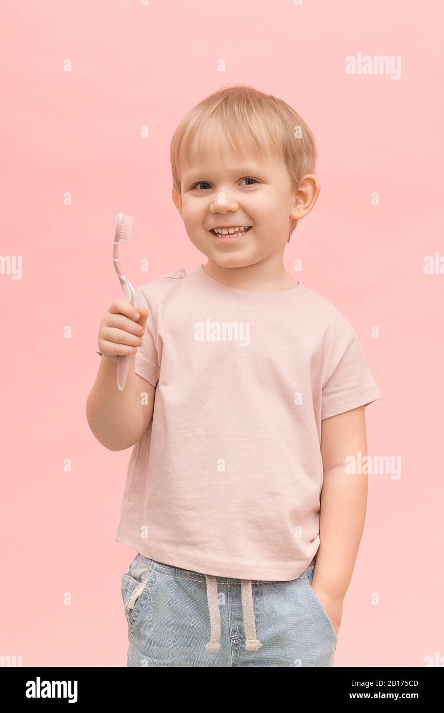 Joyeux enfant garçon blond apparence européenne tenant une brosse à dents dans ses mains sur un fond rose. Concept vertical pour les articles sur les soins buccaux et hygie Banque D'Images