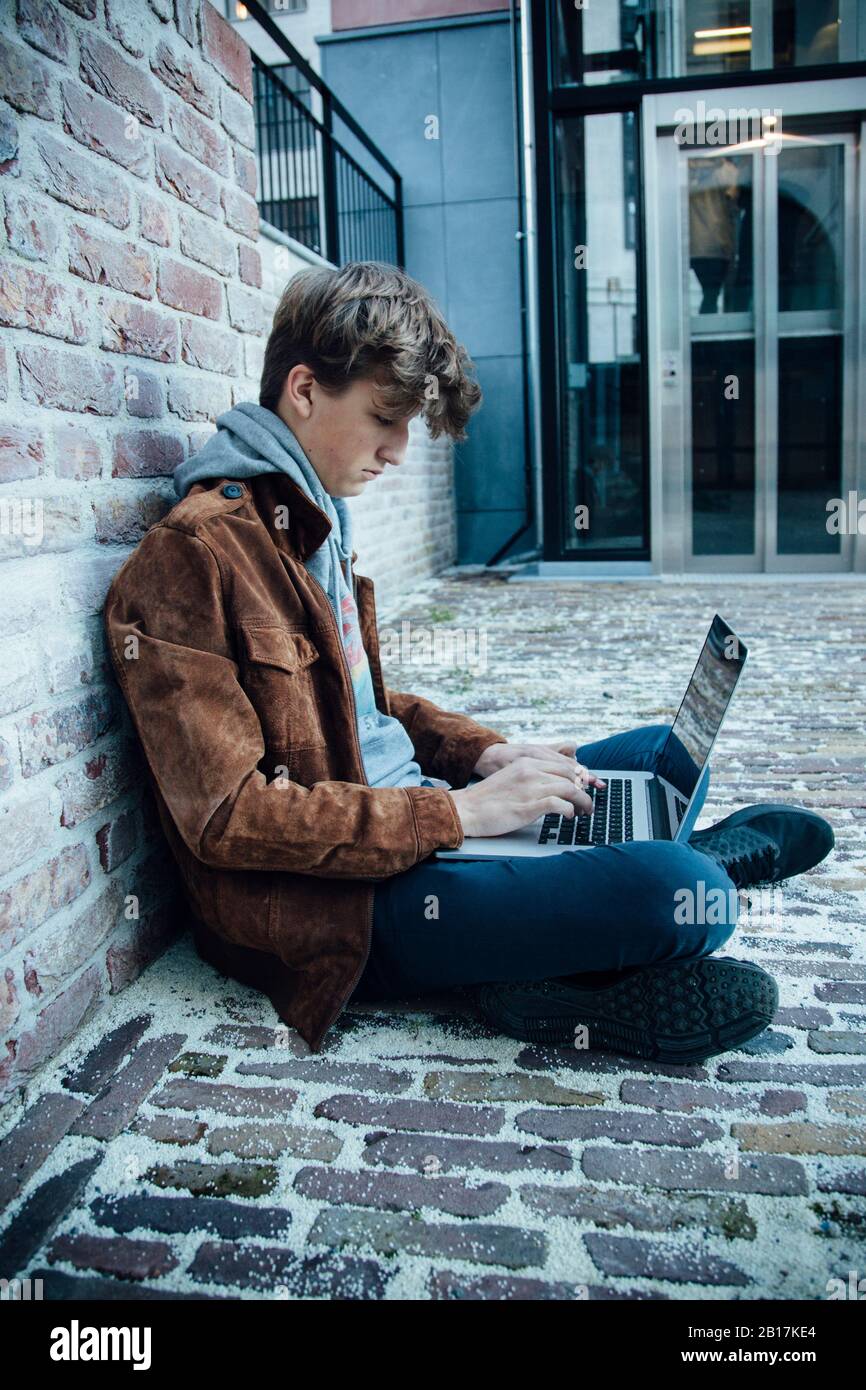 Adolescent utilisant un ordinateur portable et assis sur un sol en pierre dans la ville Banque D'Images