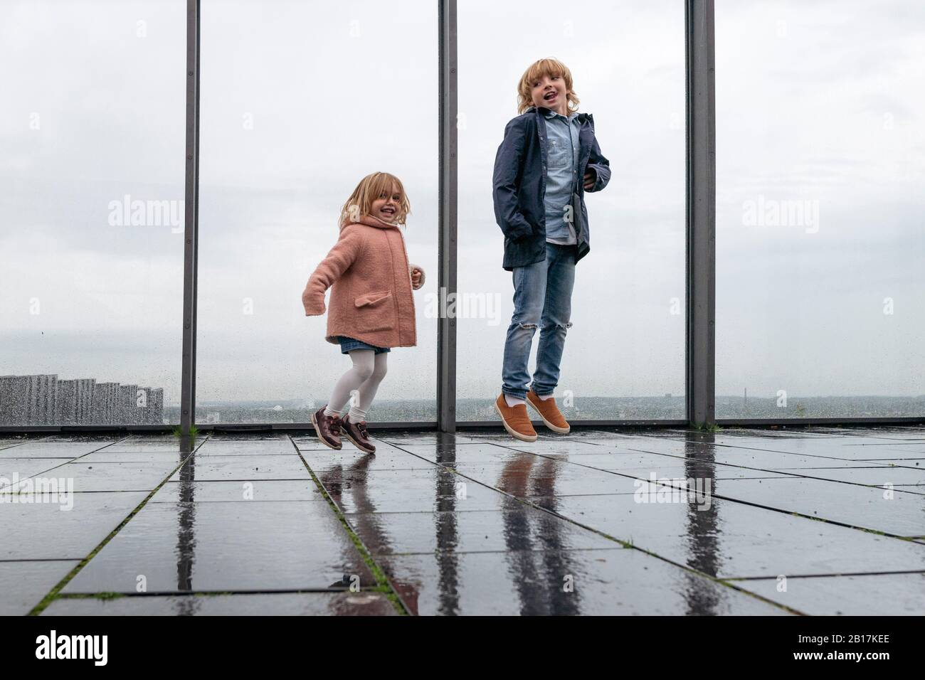 Frère et petite sœur sautant sur la terrasse avec vue le jour des pluies Banque D'Images