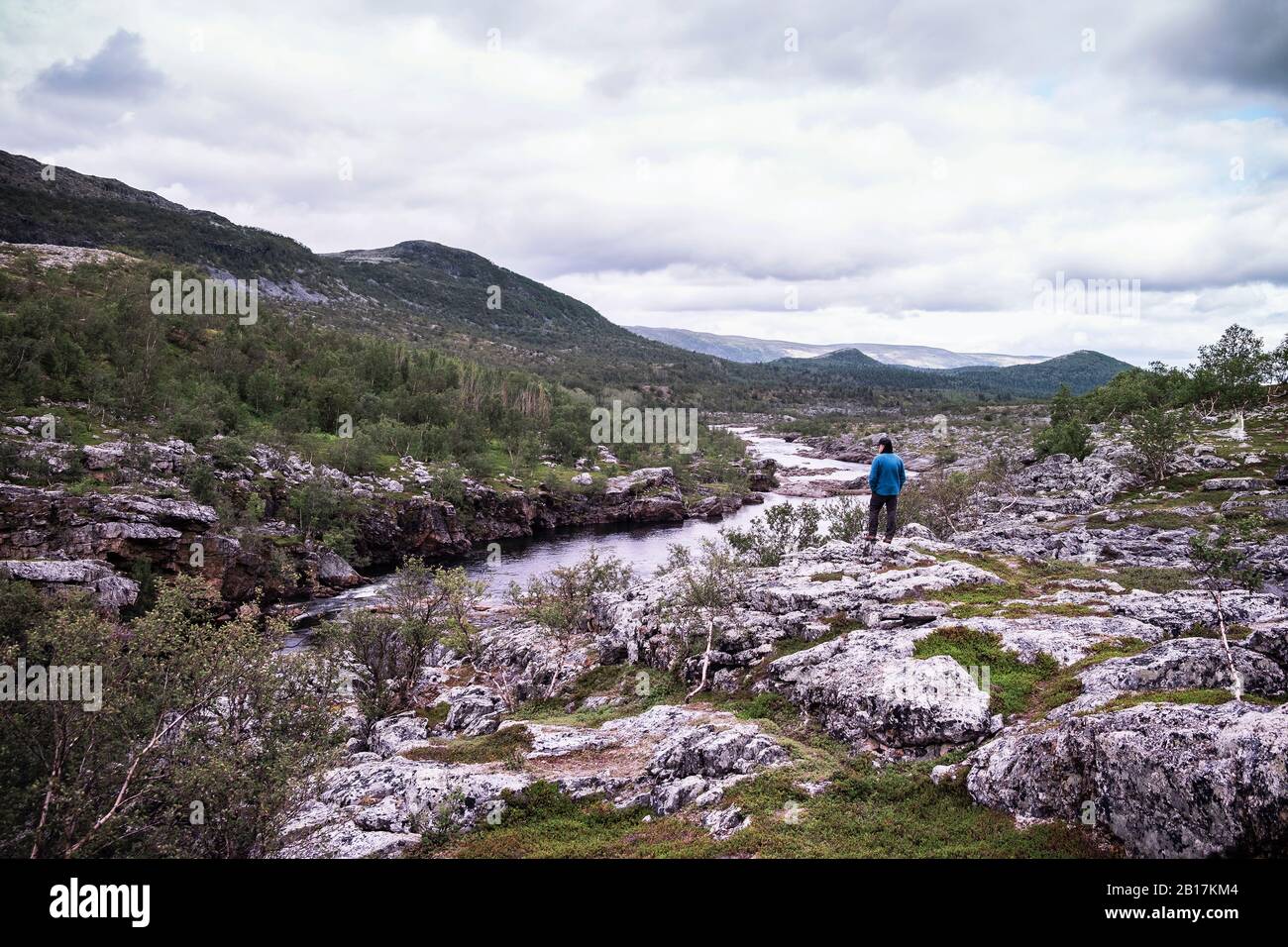Homme debout au-dessus de la rive de la rivière avec des montagnes, Lakselv, Norvège Banque D'Images