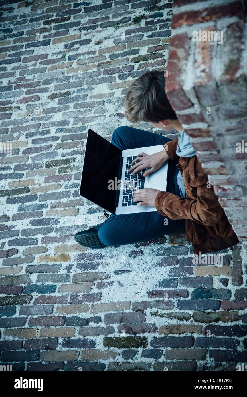 Adolescent utilisant un ordinateur portable et assis sur un sol en pierre dans la ville Banque D'Images