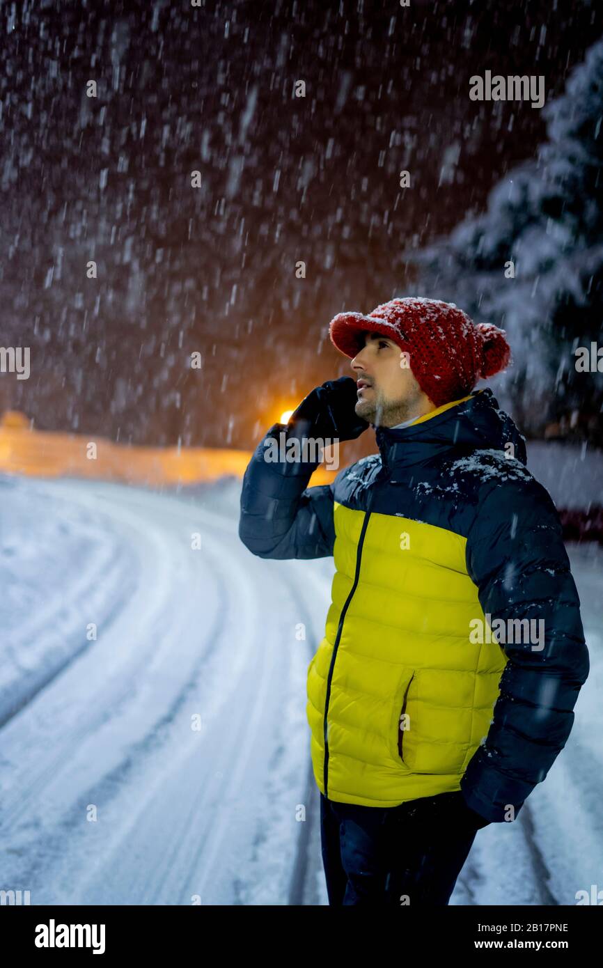 Homme au téléphone en chute de neige la nuit Banque D'Images