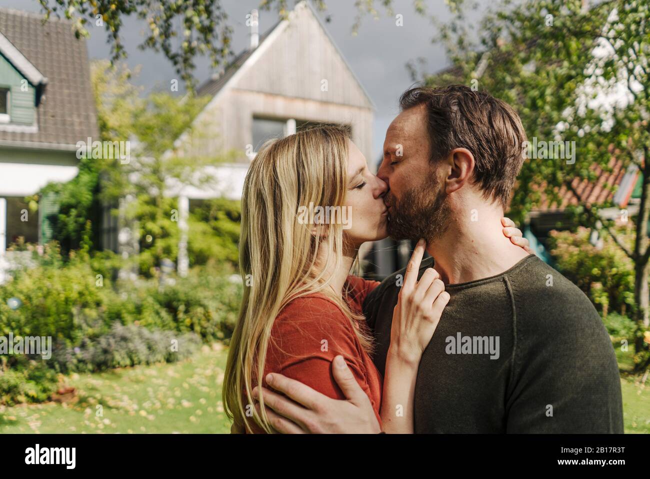 Heureux couple embrassant dans le jardin, en face de leur maison de rêve Banque D'Images