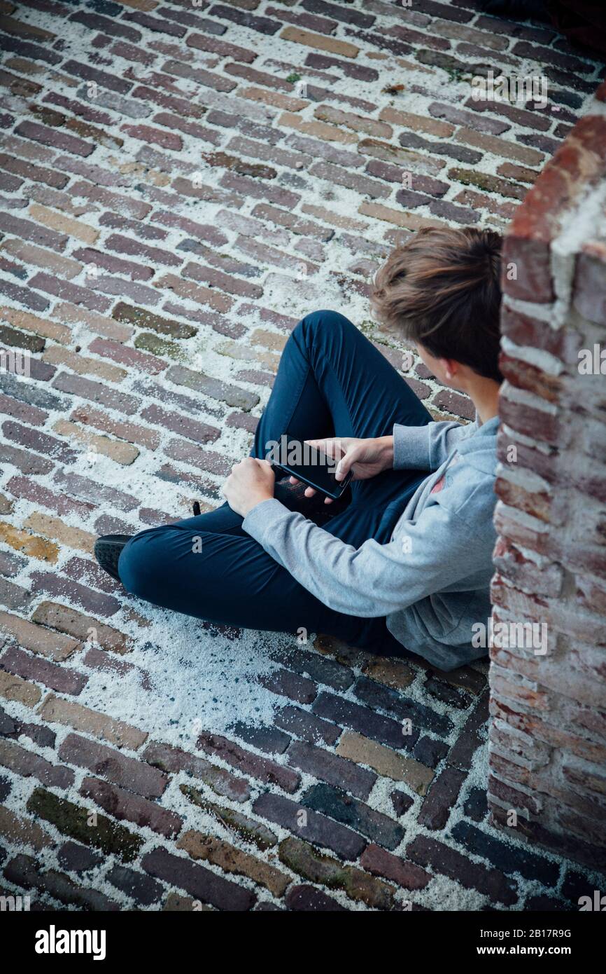 Adolescent utilisant un smartphone, assis sur un sol en pierre Banque D'Images