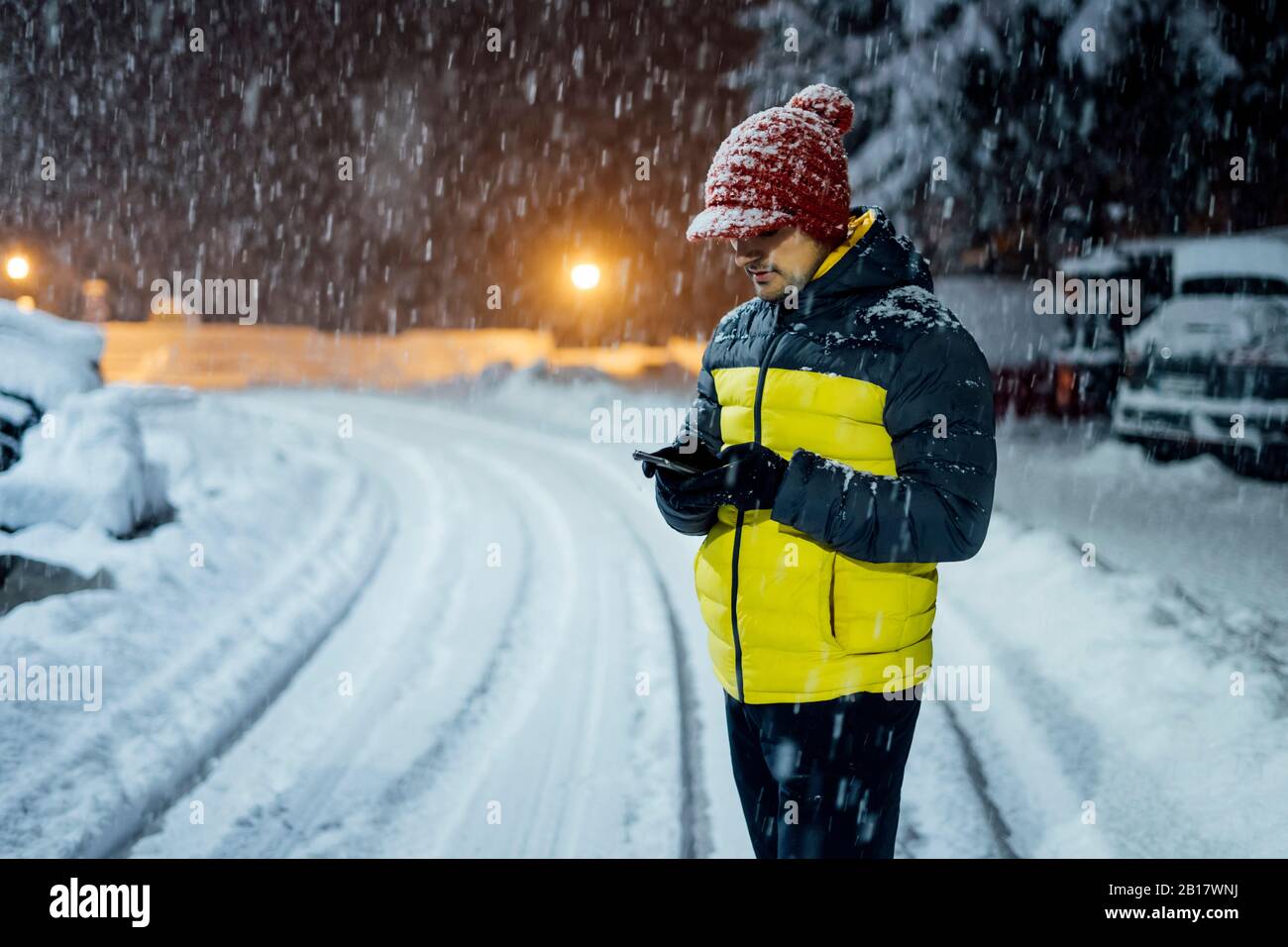 Homme utilisant le téléphone portable en chute de neige la nuit Banque D'Images
