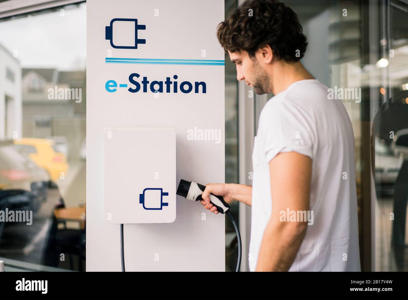 Un homme charge une voiture électrique à une station Banque D'Images