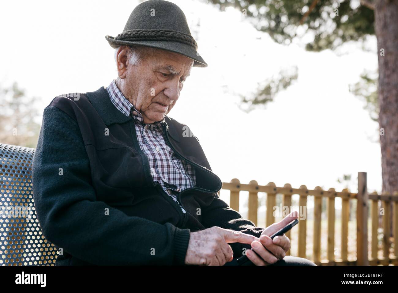 Vieil homme avec, assis sur banc, à l'aide d'un smartphone Banque D'Images