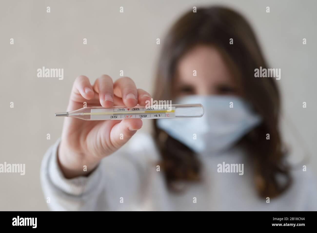 Coronavirus COVID-19 concept de quarantaine épidémique de petite fille dans un masque médical contenant un thermomètre à haut niveau de température Banque D'Images