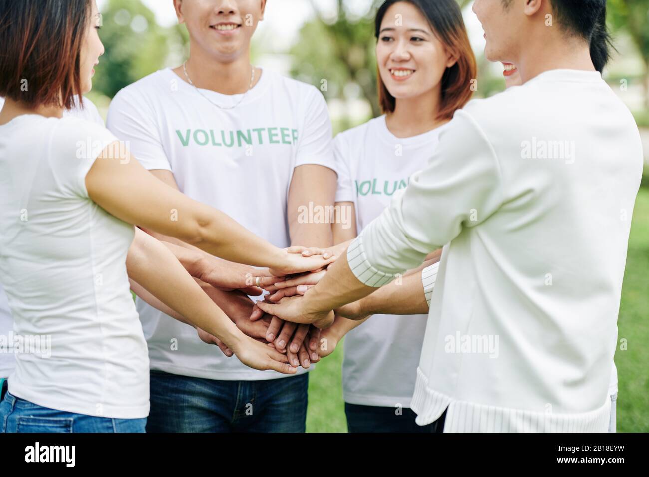 Groupe de volontaires se superposer les mains avant de s'engager avec enthousiasme dans des activités de nettoyage dans le parc local Banque D'Images