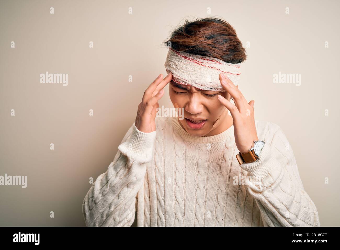 Un jeune homme chinois blessé à la main pour un accident portant un bandage et des bandes sur la tête avec des maux de tête parce que le stress. Migraine souffrant. Banque D'Images