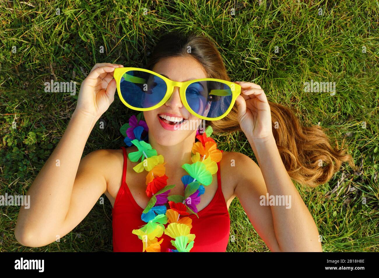 Une fille se réveille sur l'herbe après la fête du Carnaval. Jeune femme  avec garde carnaval contient de grandes lunettes de soleil drôles sur  l'herbe Photo Stock - Alamy