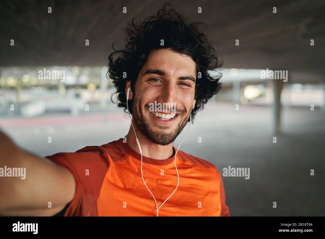Portrait d'un jeune homme souriant avec des écouteurs dans ses oreilles prenant selfie dehors - pov photo d'un homme regardant l'appareil photo souriant prendre un Banque D'Images