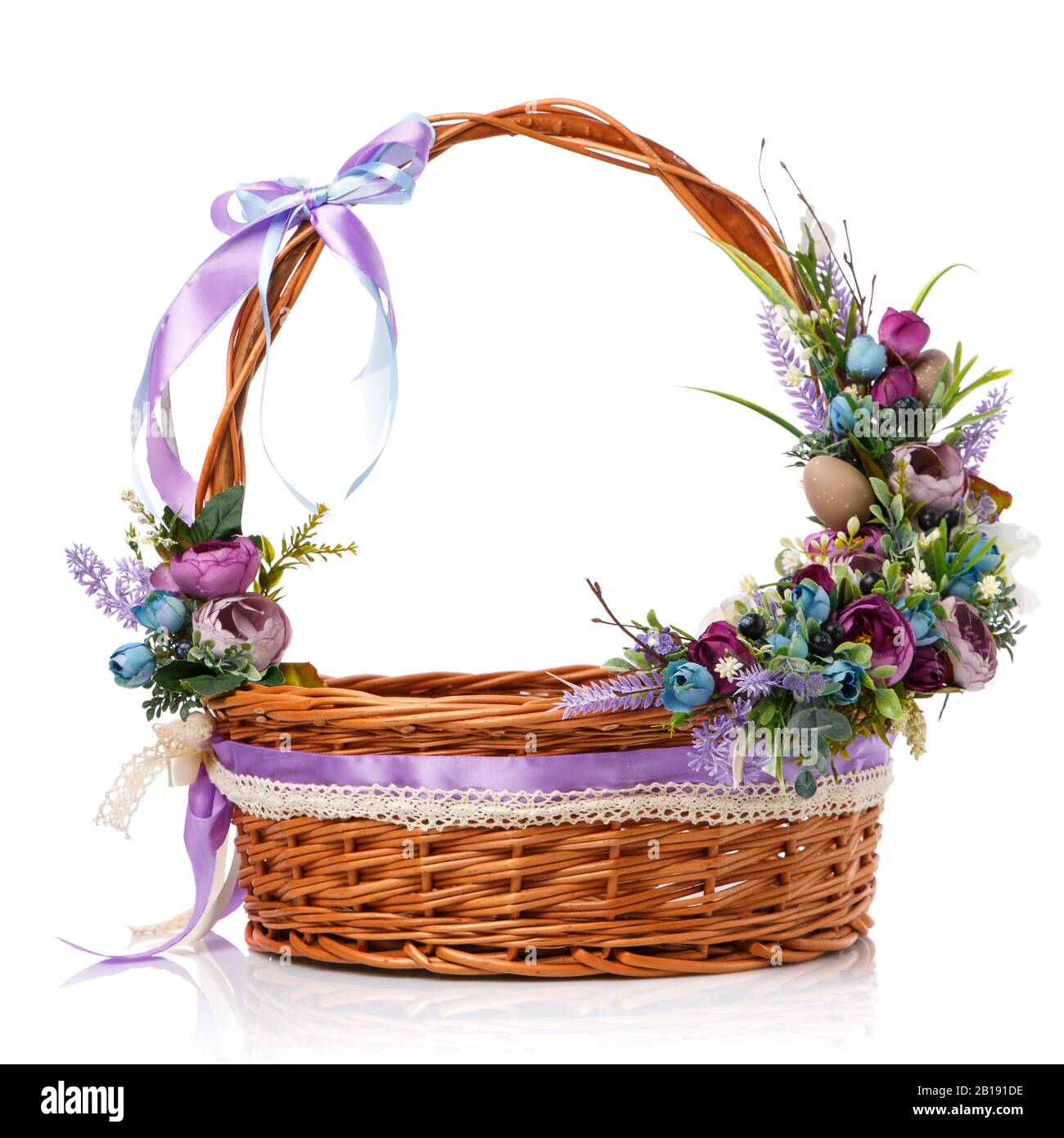 Composition florale avec fleurs, verdure et rubans accrochés sur la poignée d'un panier en osier sur fond blanc Banque D'Images