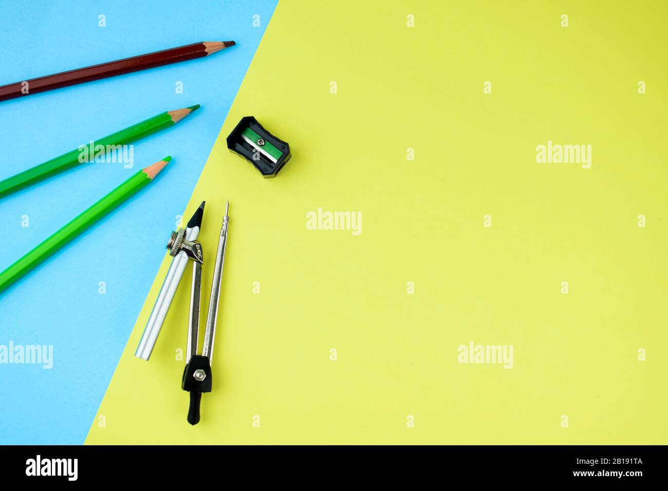 Trois crayons de couleur différents le long d'un aiguiseur-crayon noir et  d'un crayon attaché à un compas-crayon dispersé sur du papier jaune-bleu  Photo Stock - Alamy