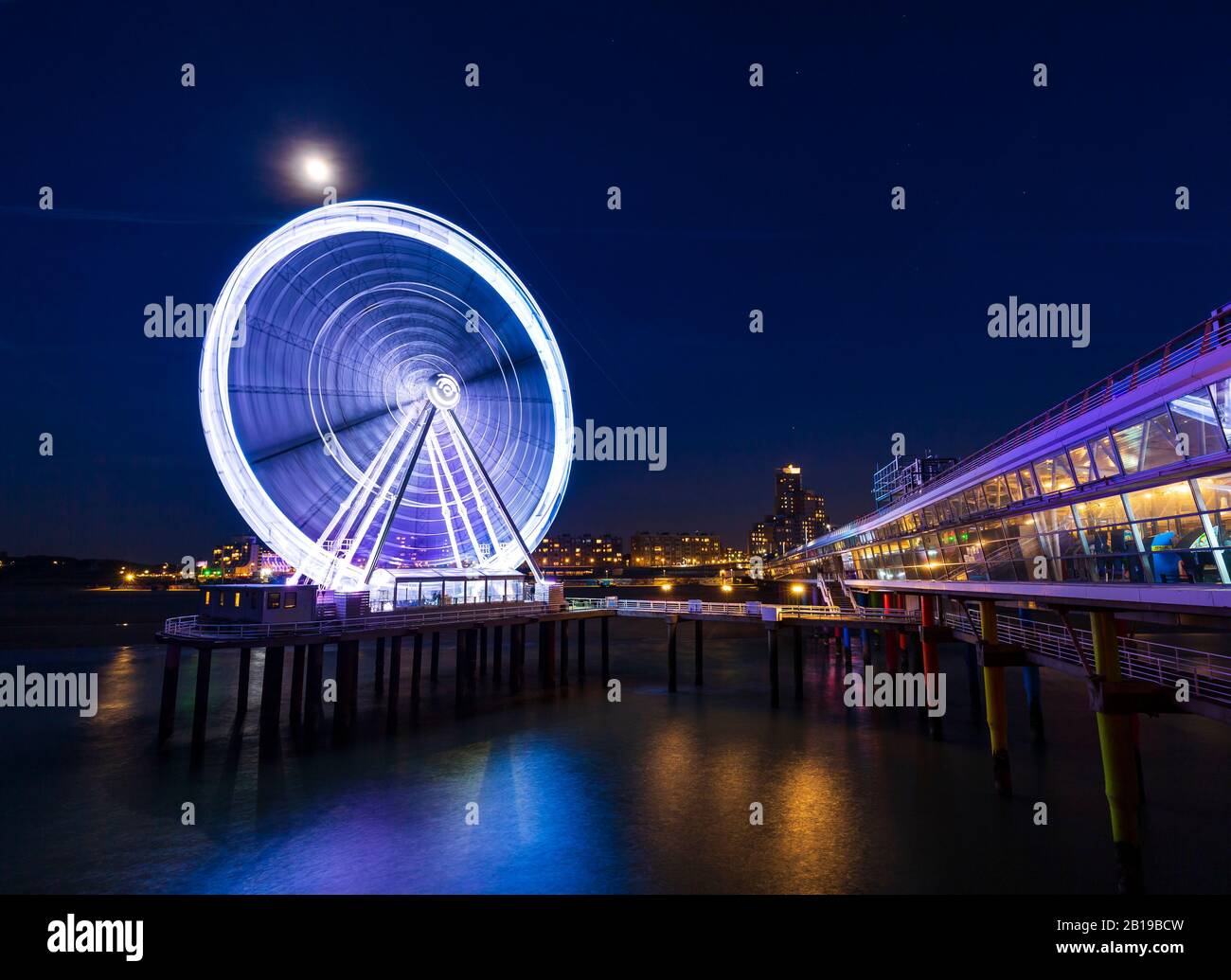 Grande roue illuminée sur la jetée de nuit sous la lune. Scheveningen, à la Haye sur l'arrière-plan, popular tourist destination. Banque D'Images