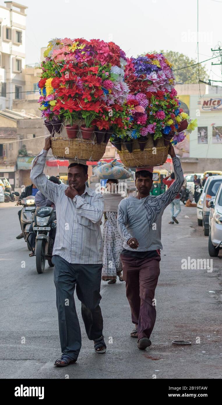 Jamnagar, Gujarat/Inde - décembre 18 2018 : deux hommes marchent dans une rue en béton très fréquentée, portant de grands paniers de fleurs colorées sur leur tête. Banque D'Images