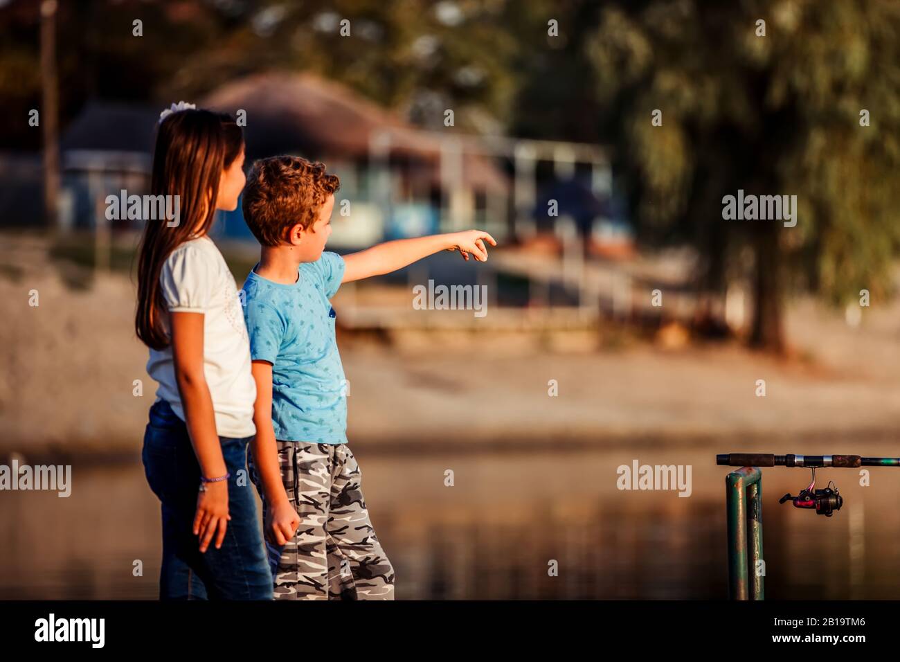 Deux jeunes petits amis mignons, un garçon et une fille pointant avec le doigt sur un lac lors d'une journée d'été ensoleillée. Les enfants jouent. Amitié. Banque D'Images