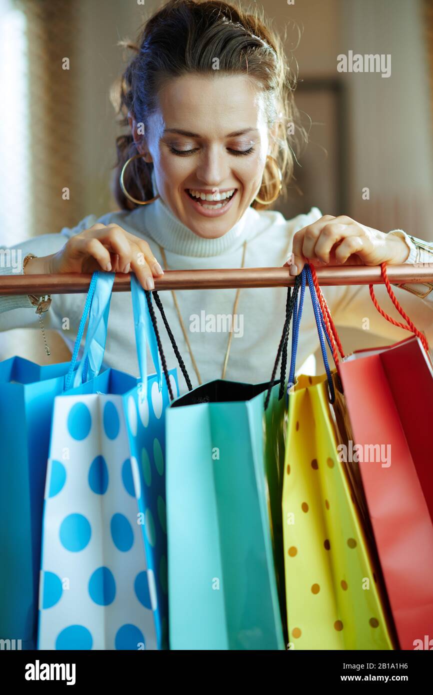 heureuse femme élégante en sweat blanc et jupe regardant dans un sac de shopping accroché sur un rail de vêtements en cuivre. Banque D'Images