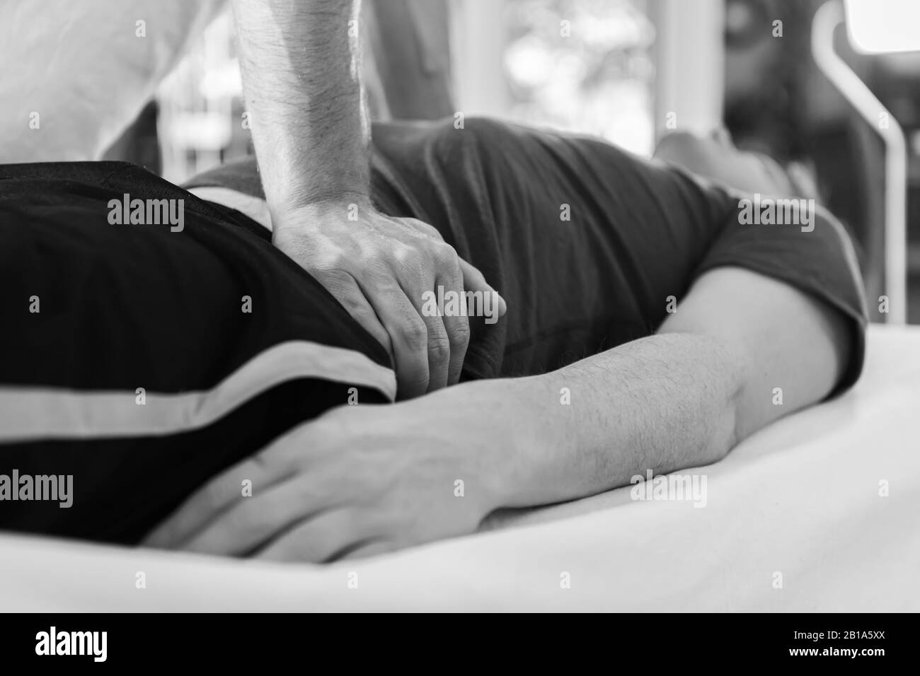 Un homme recevant un massage relaxant dans le centre thermal. Image en noir et blanc des mains de masseur non reconnaissables faisant un massage Banque D'Images