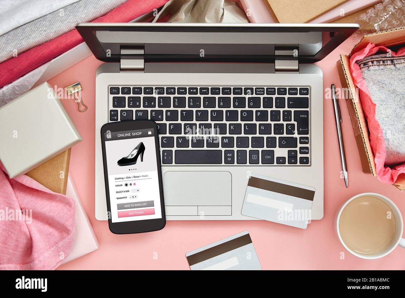 Boutique en ligne pour les femmes sur l'écran de téléphone intelligent au-dessus d'une table de bureau rose avec ordinateur portable, cartes de crédit et vêtements. Vue de dessus. Banque D'Images