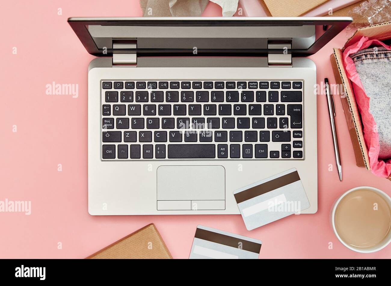 Concept de shopping en ligne sur table de bureau rose avec ordinateur portable, cartes de crédit, colis et vêtements. Vue de dessus. Banque D'Images