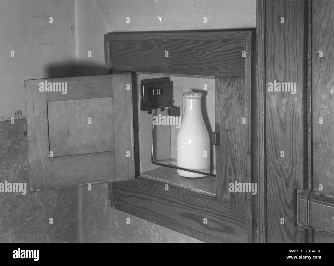 Goulotte de lait, ouverte, avec une bouteille de lait. années 1920 - 1950. Il y a une certaine contration métallique avec une barre qui maintient la bouteille en place. Moulure intérieure en bois de qualité agréable tout autour de la goulotte de lait. Ces goujures étaient habituellement construites à l'arrière de la maison, près de la porte arrière. Pour voir mes autres images anciennes, recherchez : Préstor vintage Banque D'Images
