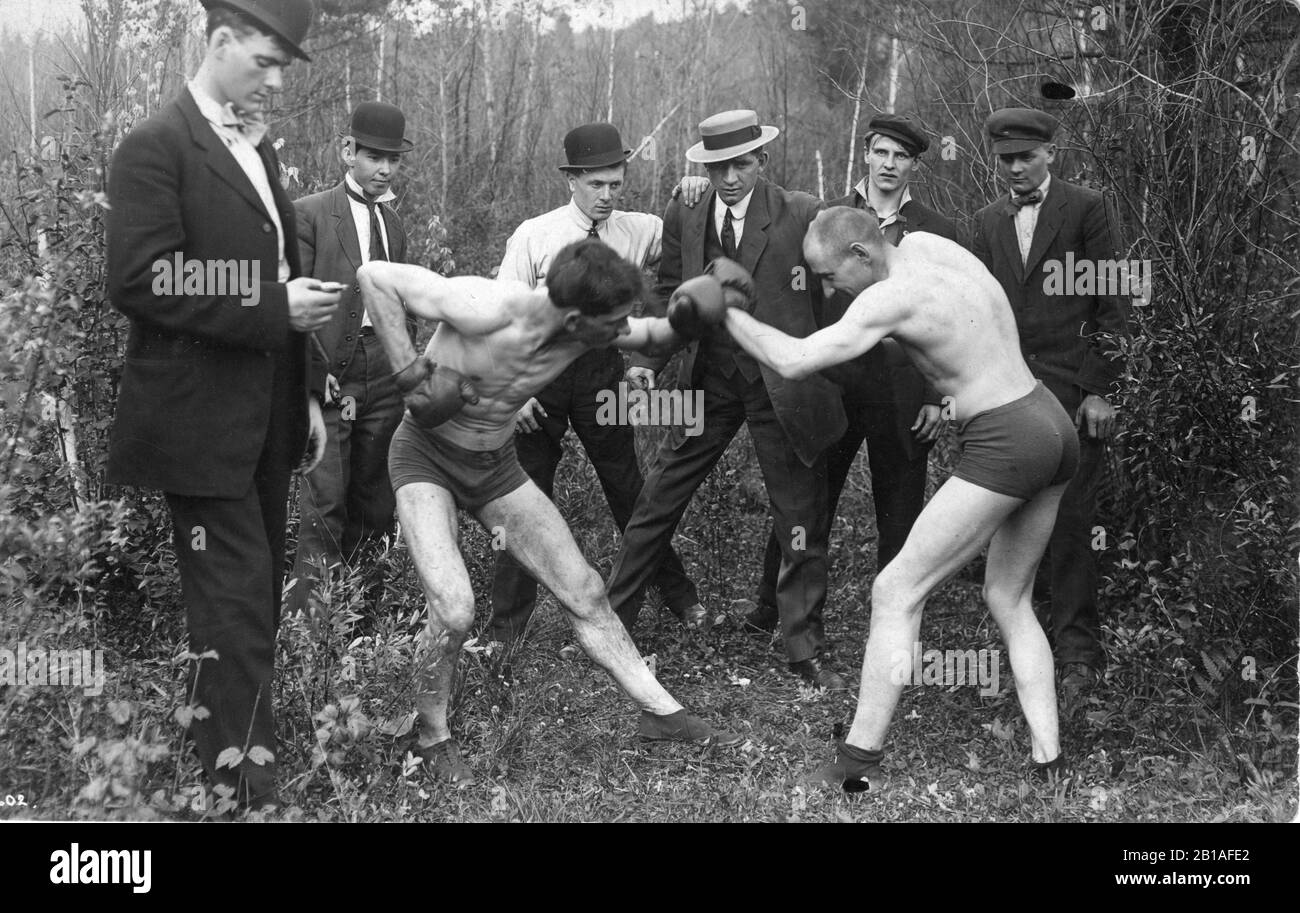 Deux jeunes hommes posent comme tho ils sont la boxe, tandis que cinq hommes les regardent, et un homme fois le combat avec un chronomètre. Les combattants ne portent que des shorts mouchés et skimy et des chaussures simples. Les deux hommes sont plutôt maigres et ont l'air expérimentés. C'est ce qui se passe en automne, c. 1909. Pour voir mes images vintage connexes, recherchez: Prestor vintage sport Banque D'Images