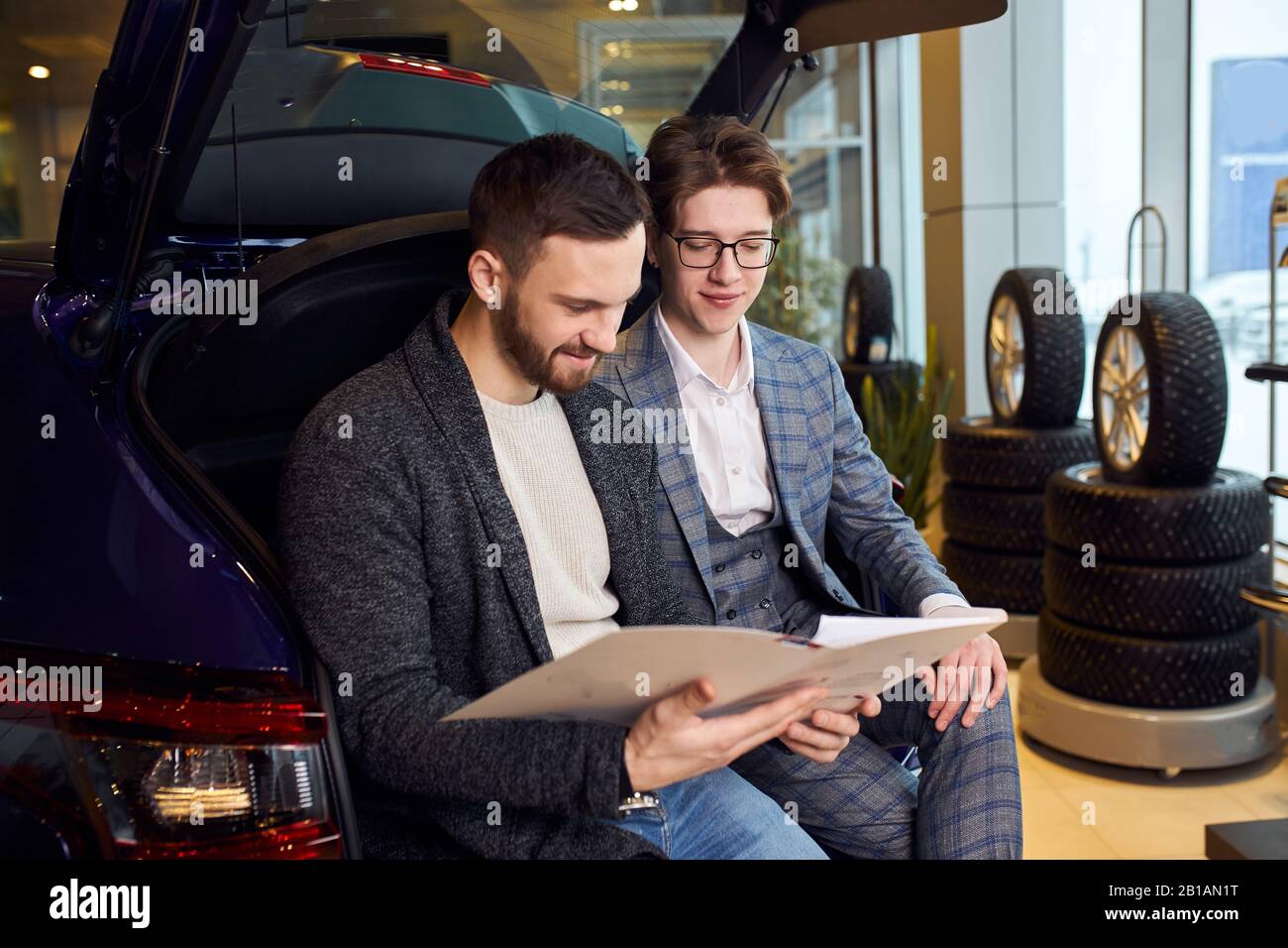 jeune homme barbu et concessionnaire lisant des documents, contrat, photo de gros plan. deux hommes apprennent les options de la voiture Banque D'Images