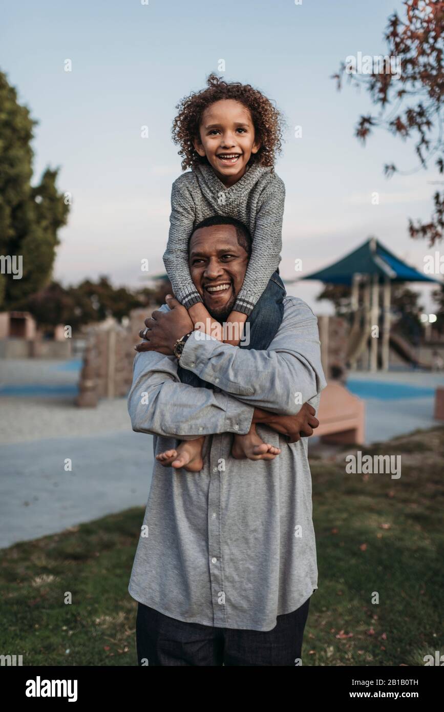 Fils joyeux assis sur les épaules d'un père heureux au terrain de jeu du parc Banque D'Images