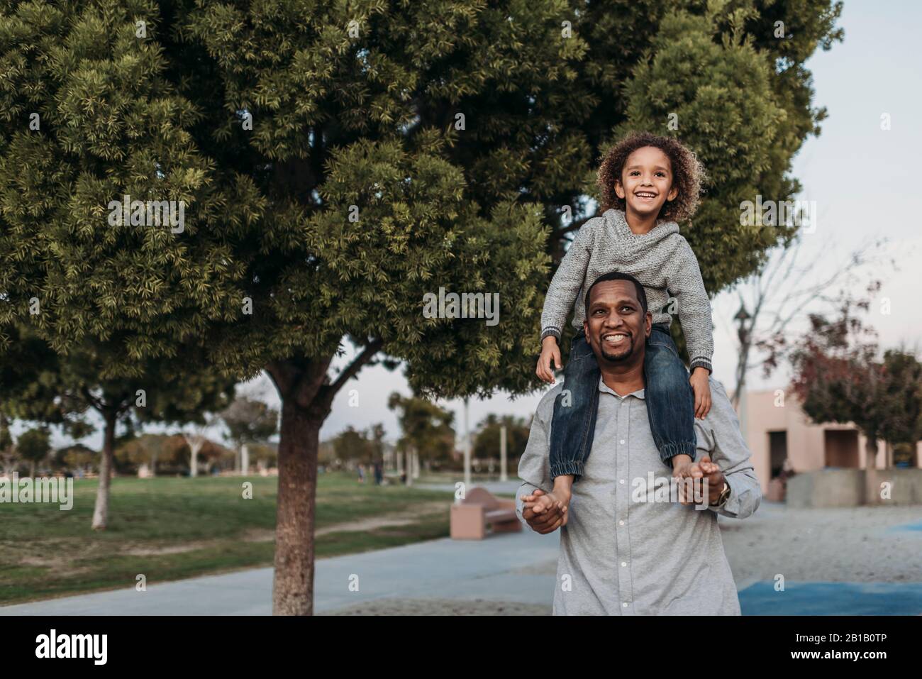 Fils joyeux assis sur les épaules d'un père heureux au terrain de jeu du parc Banque D'Images