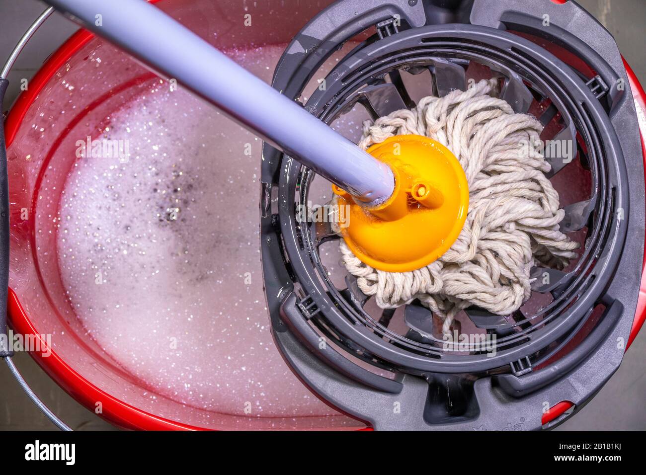 Fermer POV le dessus-de-la-tête d'une serpillière humide pressée dans un seau en plastique rouge d'eau savonneuse. Banque D'Images
