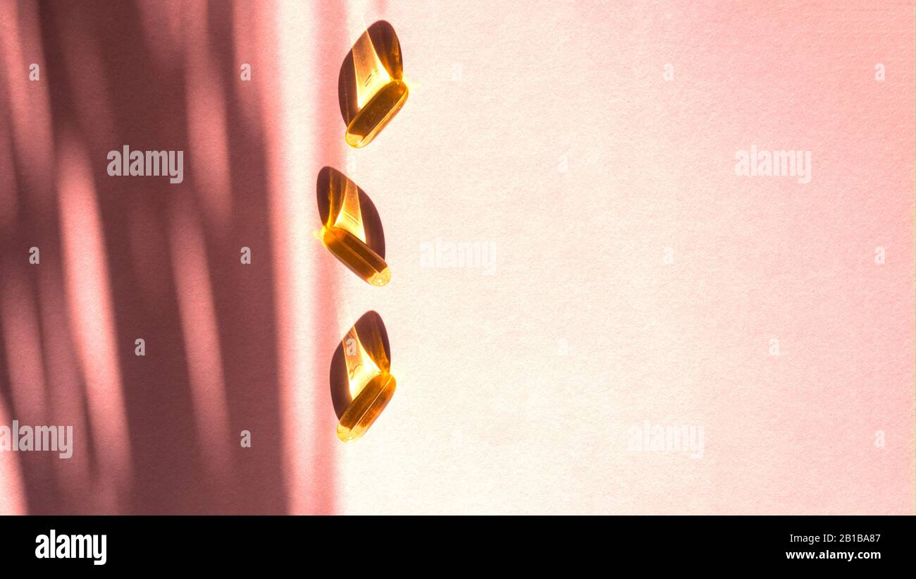 Capsules jaunes d'huile sur fond rose, vitamines et concept antioxydant Omega 3, morue du foie ou huile d'onagre du soir pour les soins de santé. Le Minimalisme. Espace de copie. Banque D'Images