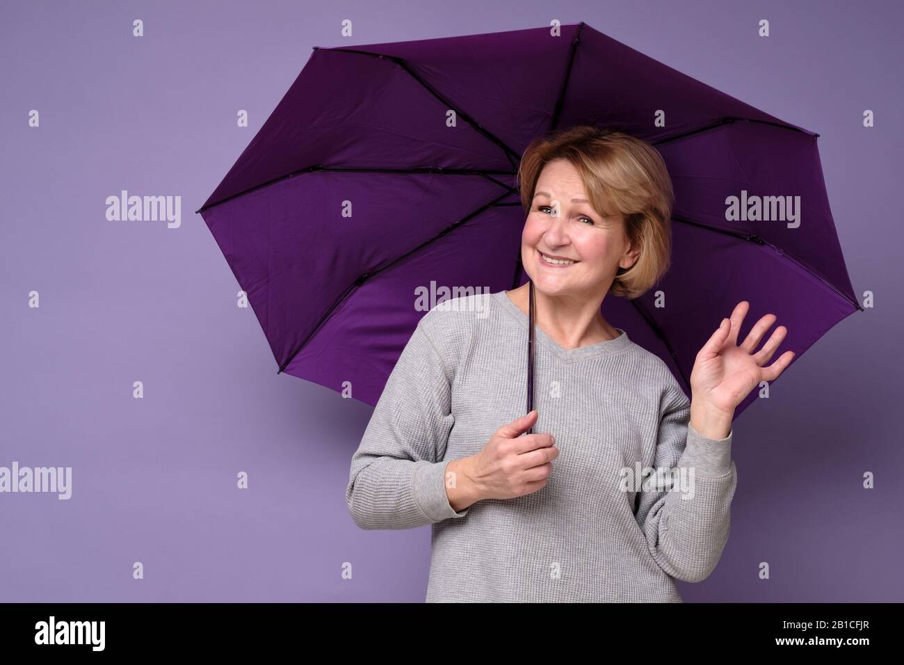 Caucasienne femme mûre se tenant heureux et détendu avec parapluie, isolé sur le mur de studio de couleur. Prêt pour la pluie de printemps. Banque D'Images